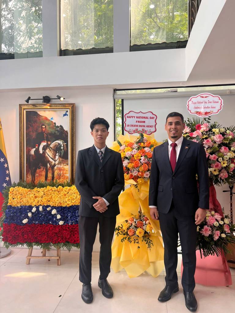 Giám Đốc Dự án TUT BRAND - Ông Nguyễn Ngọc Hưng chụp ảnh lưu niệm cùng Ngài Juan Carlos Fernandes Juárez – Đại sứ Đặc mệnh Toàn quyền nước Cộng hòa Bolivar Venezuela bên lẵng hoa chúc mừng của thương hiệu JAI & TUT – biểu tượng cho tình hữu nghị và kết nối văn hóa giữa hai quốc gia.